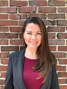 Dr. Elizabeth Inman's profile; wearing a grey blazer and maroon shirt, with a brick wall background